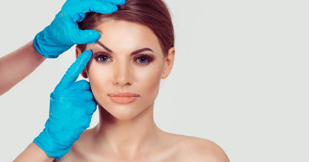 blue hand gloves touch a woman's eyelid.